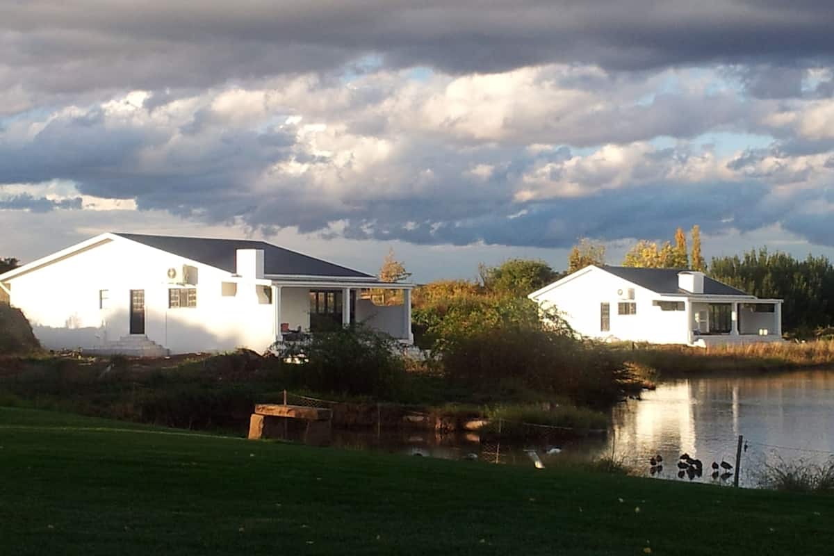 Deux maisons blanches au bord d’un lac, sous un ciel nuageux.