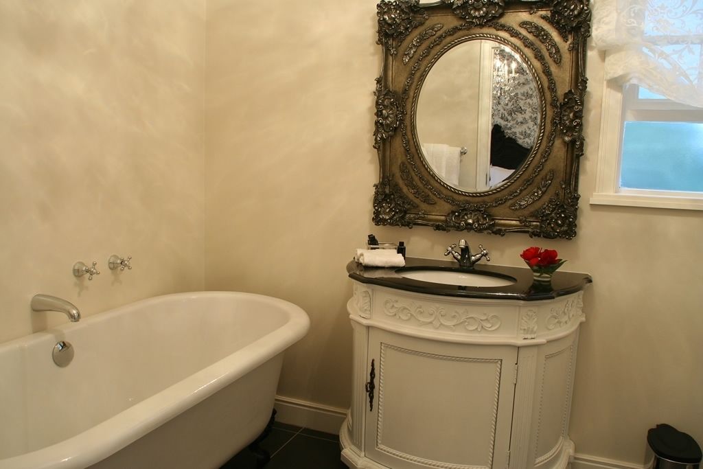 A bathroom with a white bathtub, a sink with a decorative cabinet, and a mirror with an ornate frame.