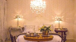 A bedroom with a bed, two bedside tables, a chandelier, and a round table with chairs. - La Riviera Guesthouse (Mohokare)