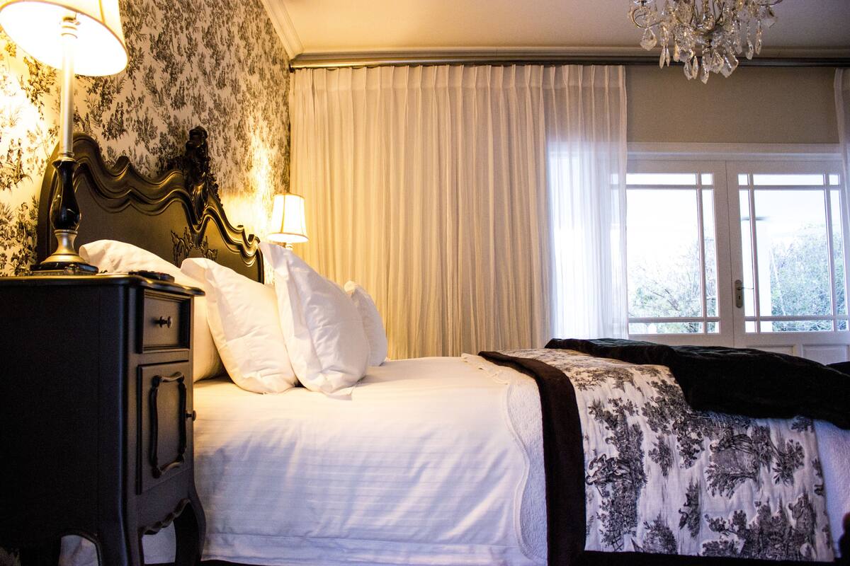 Une chambre d’hôtel avec un lit, une table de chevet, une lampe et une fenêtre avec des rideaux.