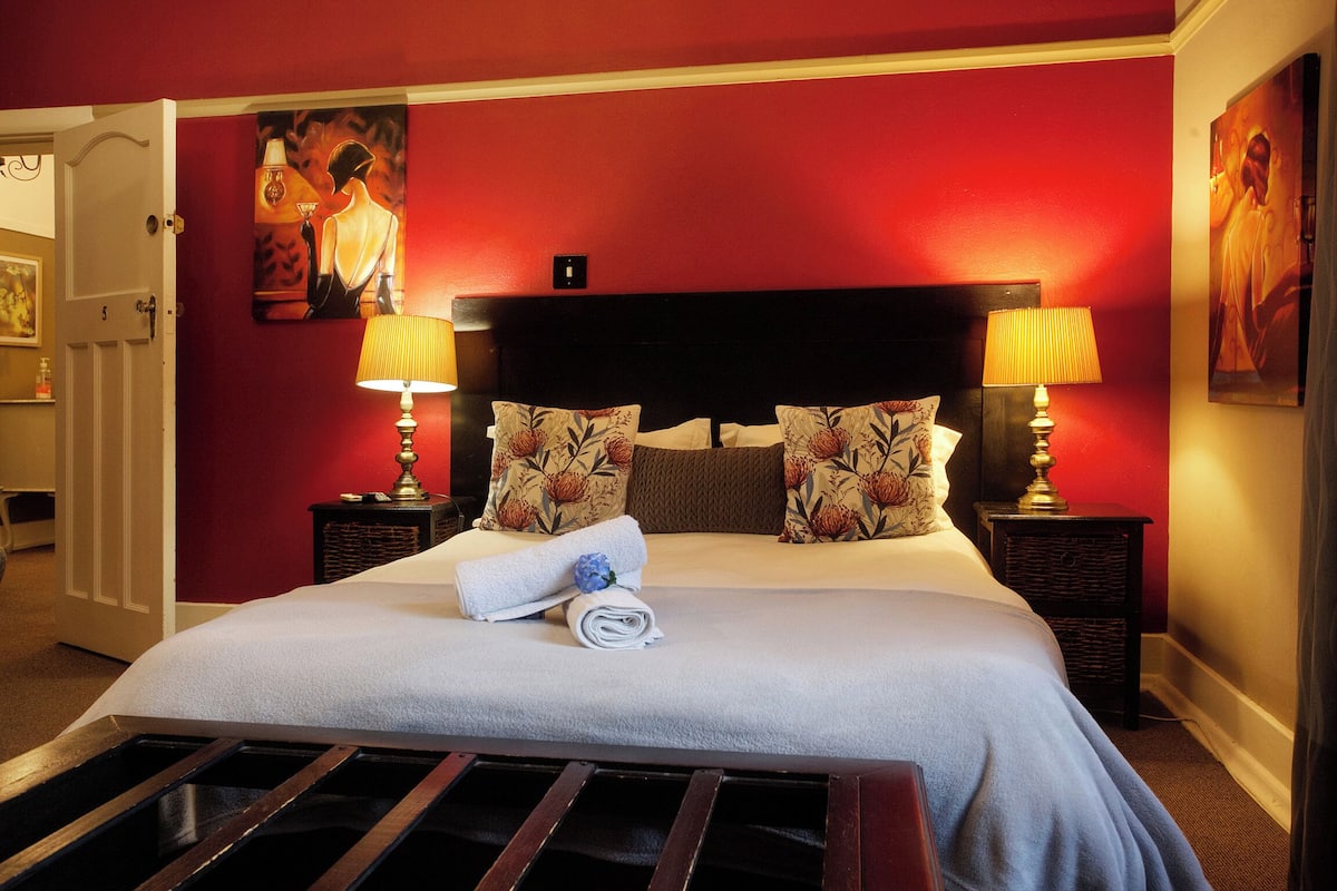 A neatly made bed with floral pillows, a rolled towel, and two bedside lamps.