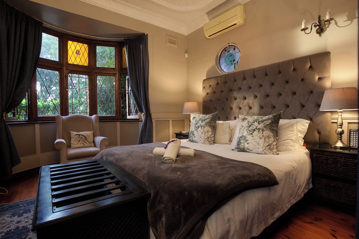 A bedroom with a large bed, a chair, a bedside table, and a window with curtains.