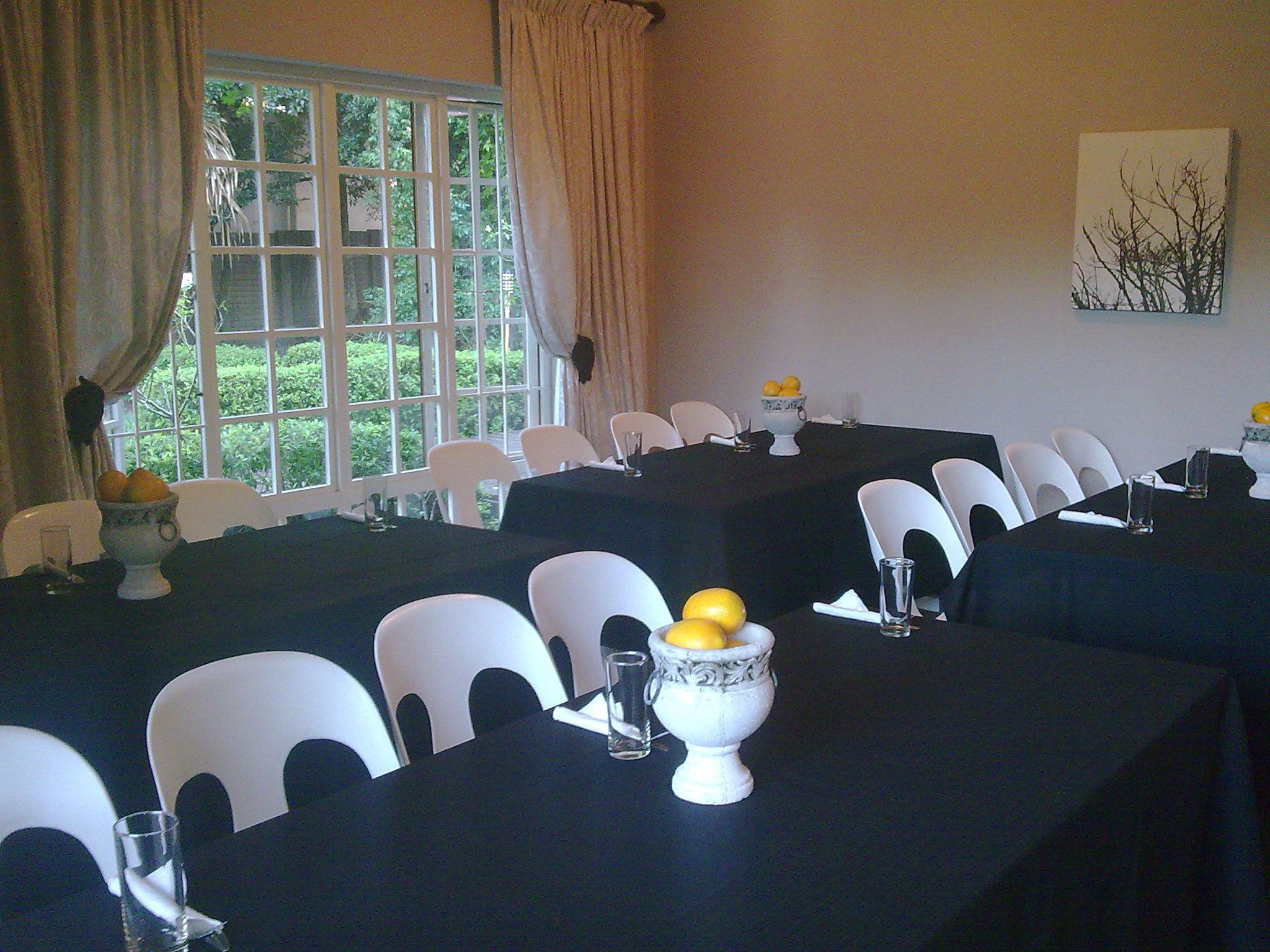 A conference room with tables set for meetings, white chairs, and a window with curtains.