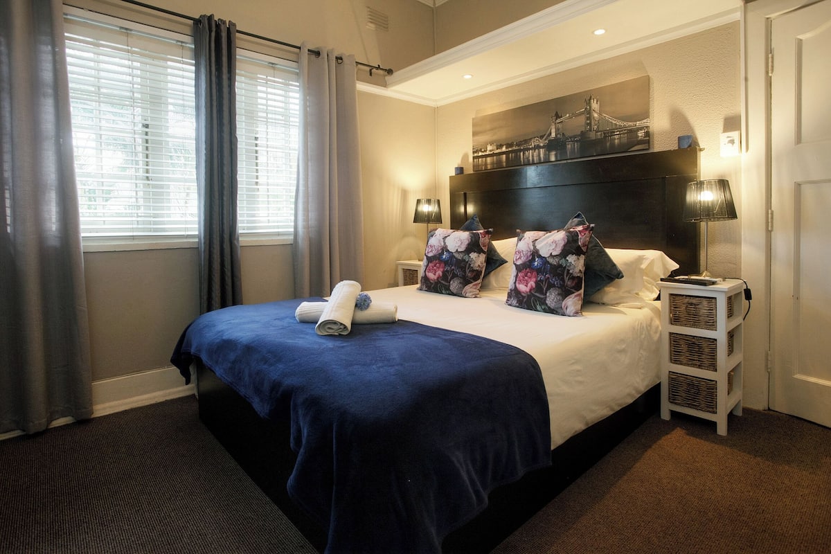 A hotel room with a large bed, two bedside tables, a nightstand, a wall-mounted TV, and a window with curtains.