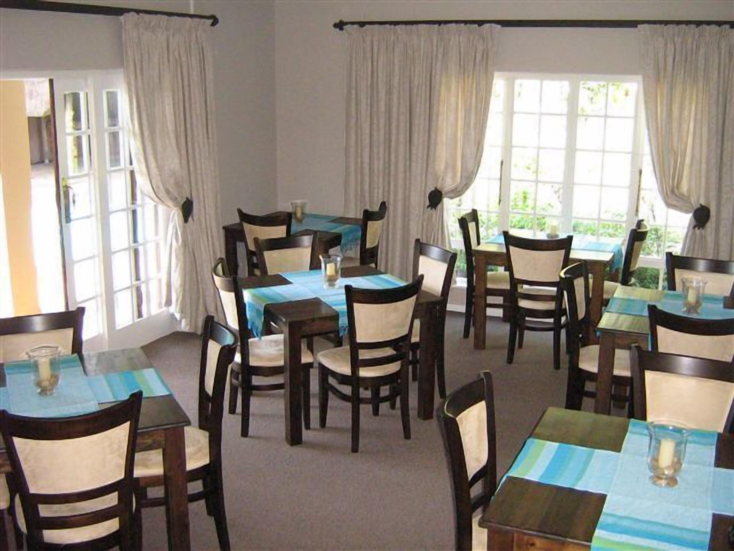 A dining area with multiple tables and chairs, large windows with curtains, and a view of greenery outside.