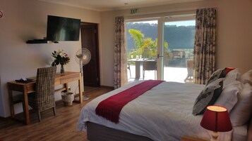 A hotel room with a bed, a desk with a computer, a TV, a fan, and a balcony with a table and chairs.
