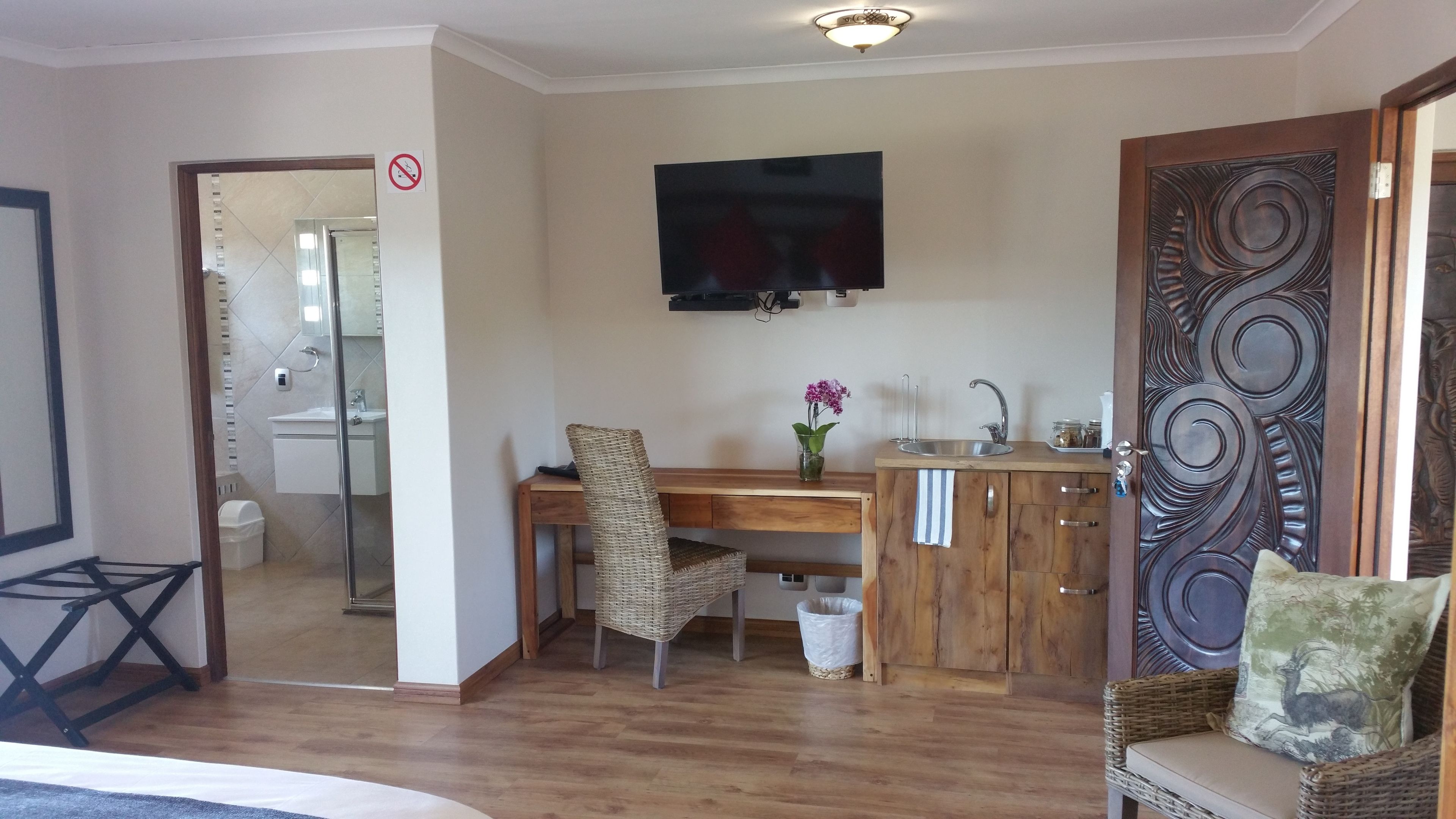 Une pièce de taille modeste, avec un bureau en bois, une chaise, un téléviseur fixé au mur, un lavabo et une porte décorative.