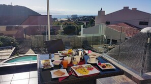 A rooftop dining area with a pool, breakfast buffet, and a view of the city and sea. - Lala Panzi B&B (Plettenberg Bay)