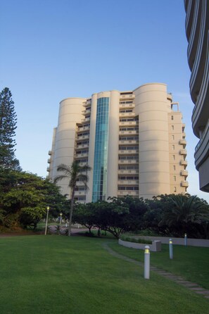 Un edificio de gran altura con varios balcones, rodeado por un césped cuidado y árboles.