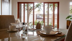 A dining area with a table set for two, featuring a clear view of the outdoors through large windows. - Organic Stay Guesthouse (Swakopmund)