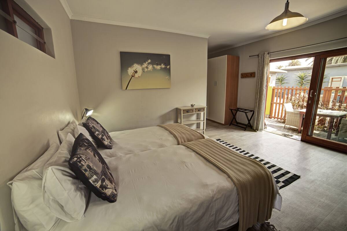 Une chambre à coucher avec un lit, une table de chevet, une commode, un tableau et une vue sur l’extérieur.