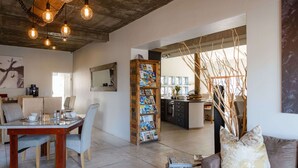 A spacious living area with a dining table, chairs, a sofa, and a bookshelf. - Organic Stay Guesthouse (Swakopmund)