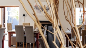 A modern dining area with wooden floors, a high ceiling, and natural light from windows. - Organic Stay Guesthouse (Swakopmund)