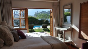 A bedroom with a large bed, a desk, and a view of a swimming pool and garden. - Dunstone Country House (Wellington)