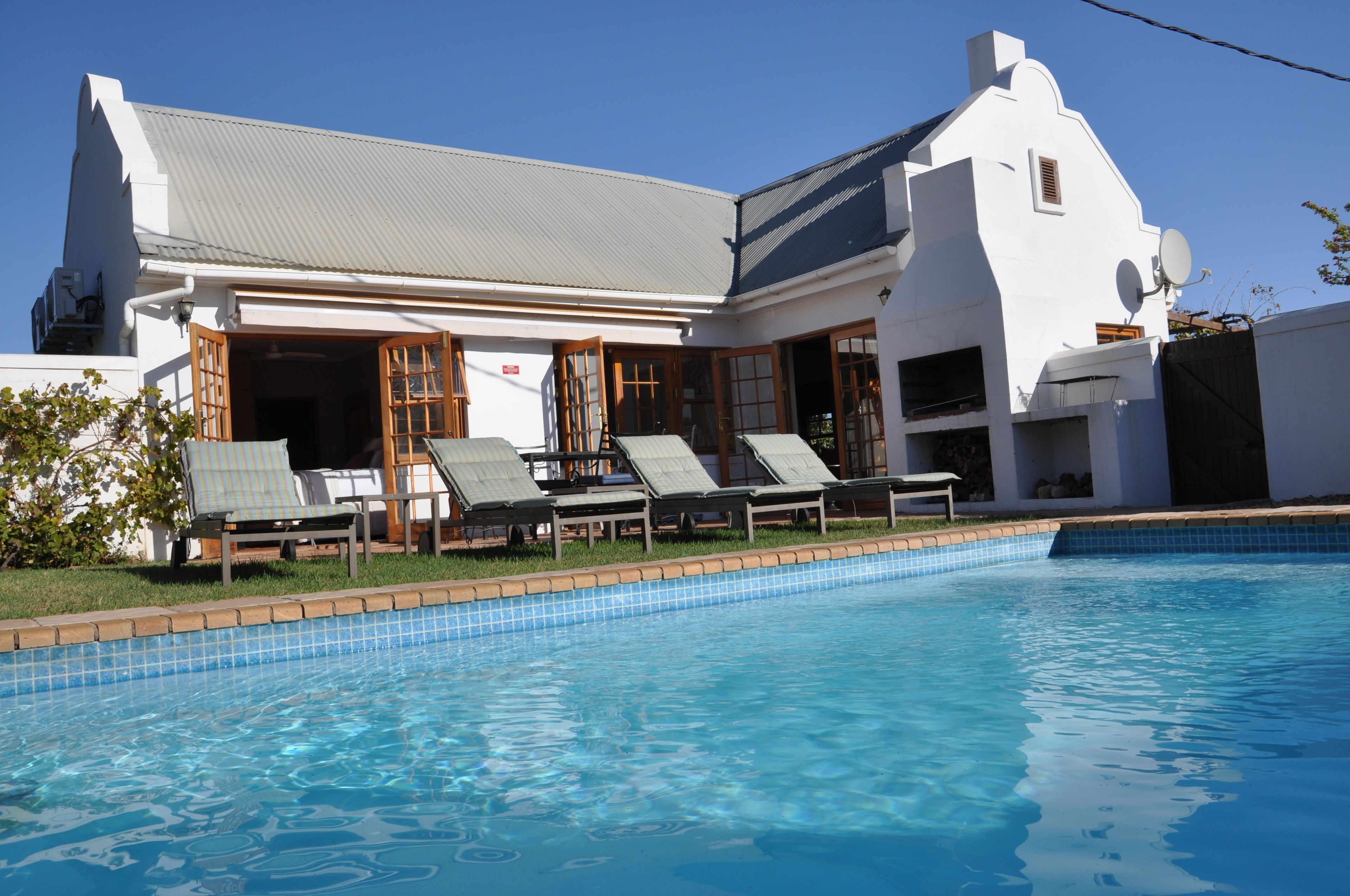 A white building with a swimming pool, sun loungers, and a covered patio area.