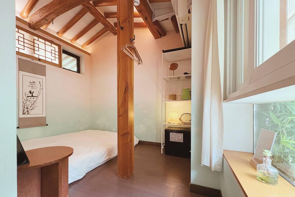 Une petite pièce agréable et chaleureuse, avec un plafond en bois, un lit, un bureau et une fenêtre donnant sur un paysage verdoyant.
