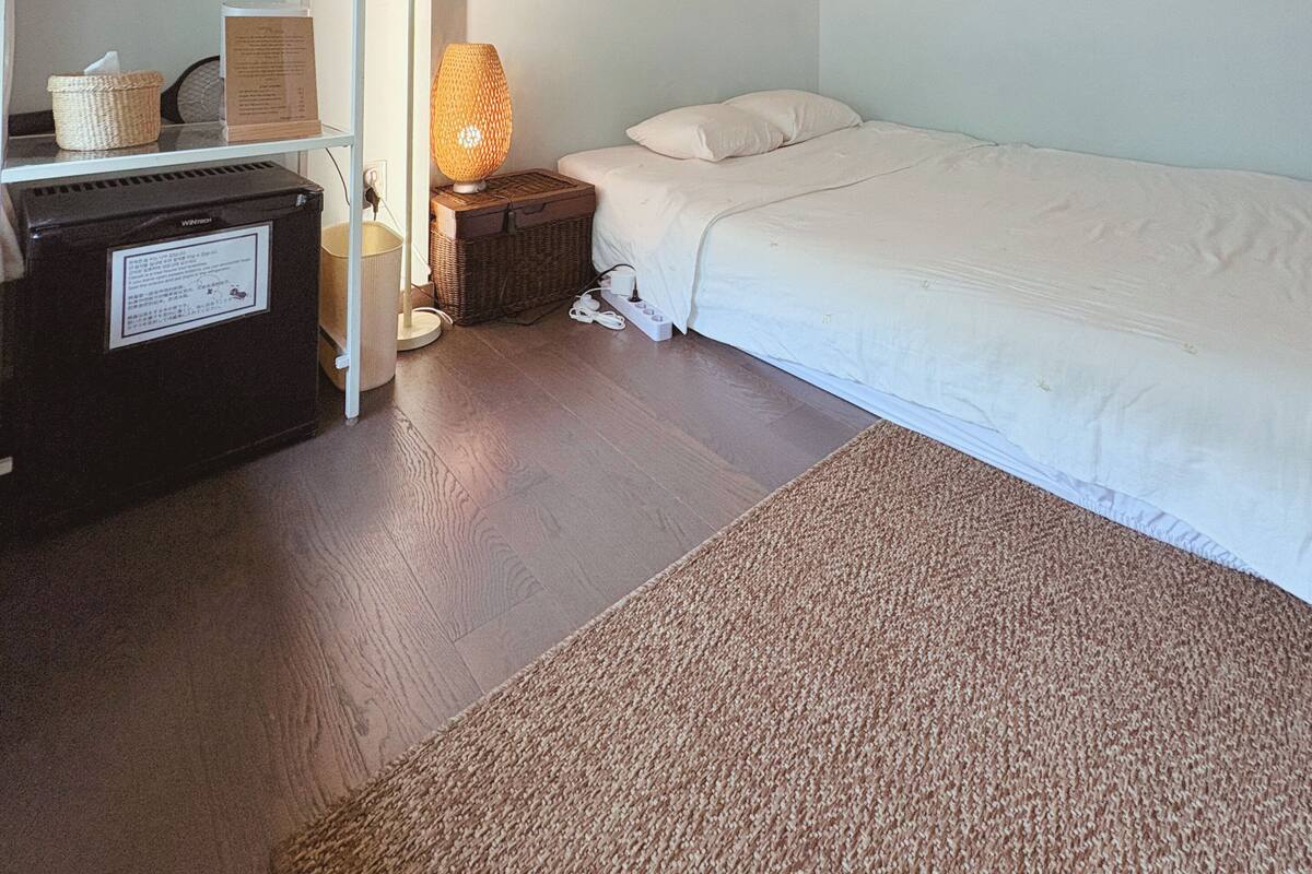 Une chambre à coucher comprenant un lit, une table de chevet, une lampe, une étagère avec divers objets et un plafond en bois.