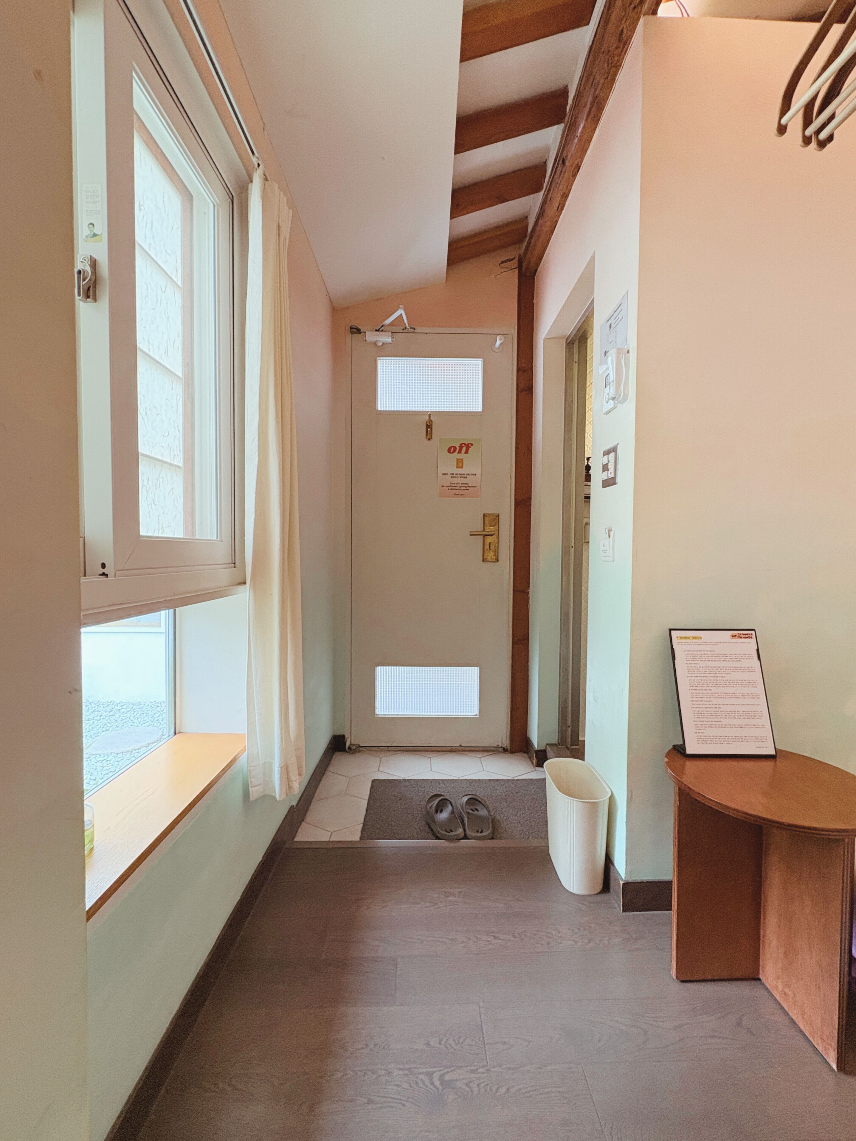 A hallway with a wooden floor, a door with a 'no entry' sign, and a window with curtains.