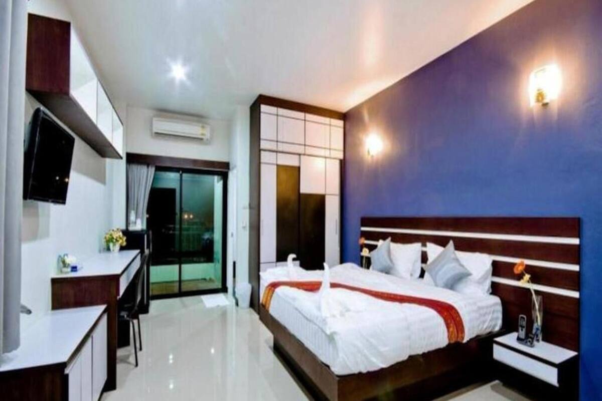 A modern hotel room with a large bed, a desk, a flat-screen TV, and a sliding glass door to the balcony.