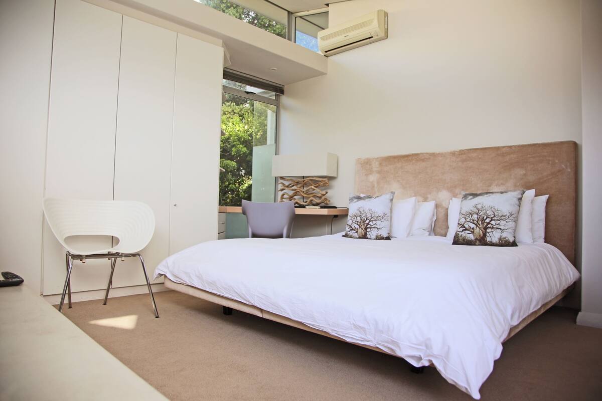 A bedroom with a large bed, a desk, a chair, and a wardrobe.