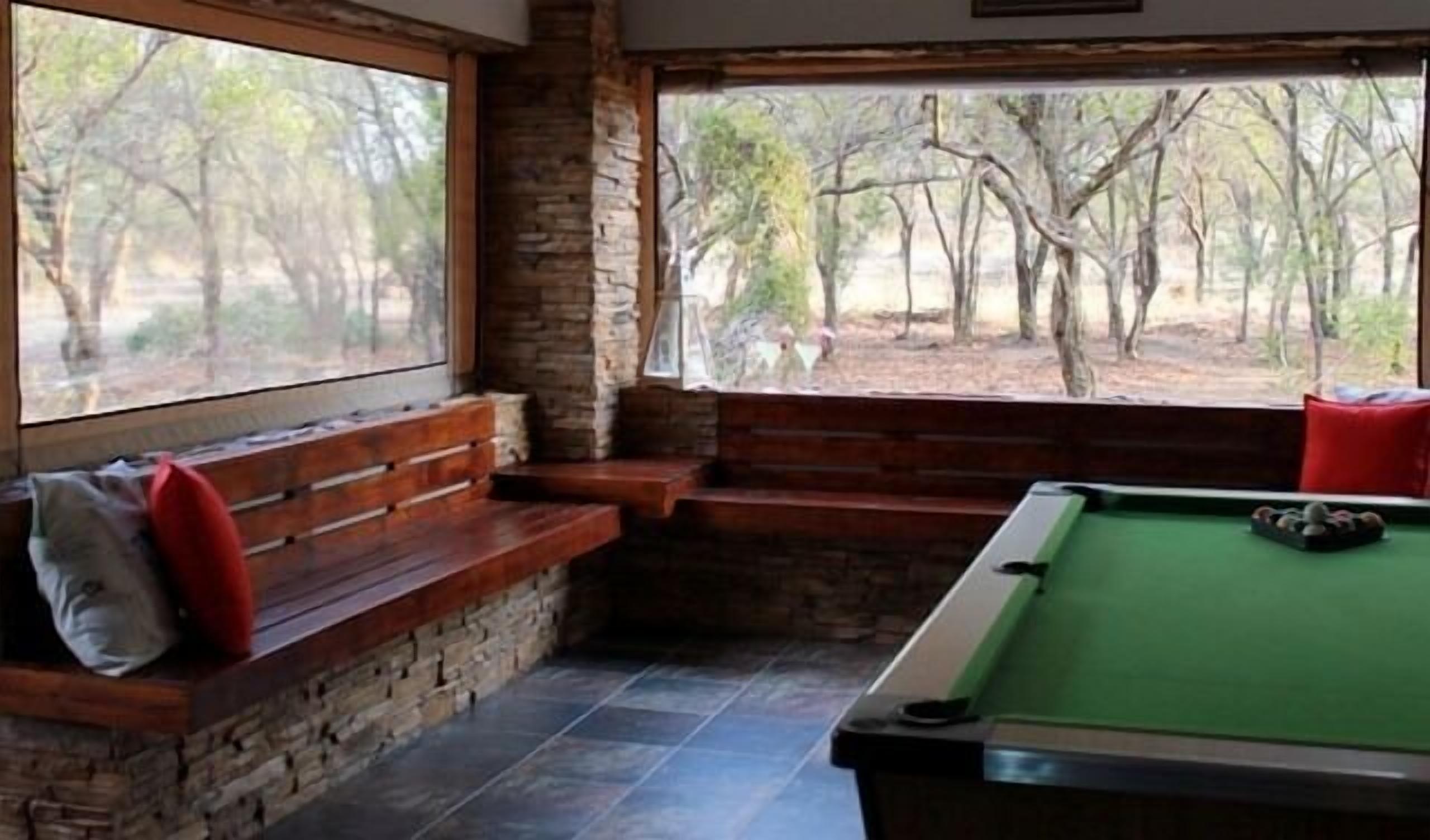 A pool table with a green felt surface, a wooden bench with red cushions, and a stone wall.