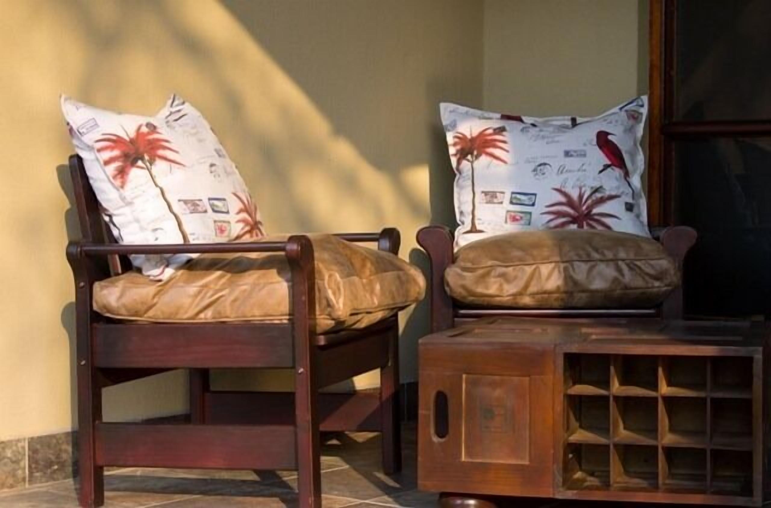 Deux chaises en bois, dotées de coussins en cuir et de coussins décorés, sont placées contre un mur.
