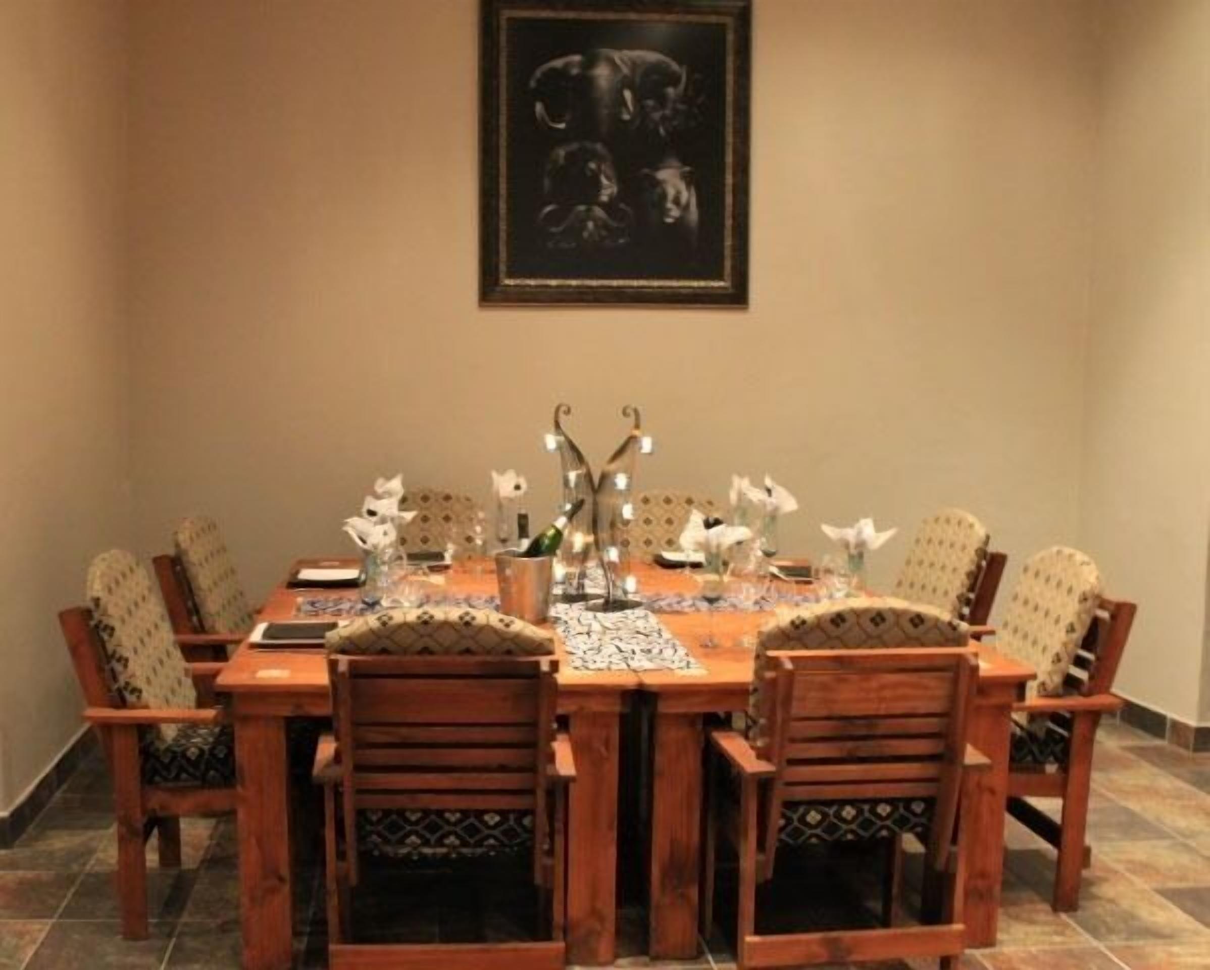 Un coin repas avec une table et des chaises en bois, un tableau encadré au mur et une bouteille de champagne posée sur la table.