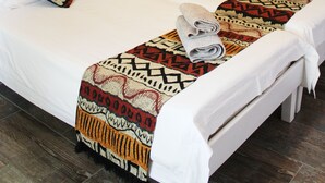 A neatly made bed with patterned pillows and a blanket, a lamp, and a wall-mounted animal hide. - Omaruru Guesthouse (Omaruru)