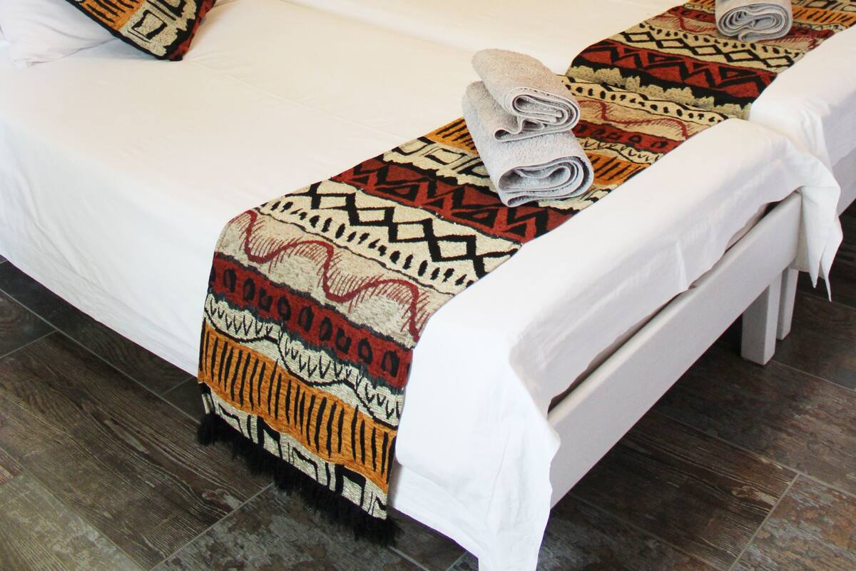 A neatly made bed with patterned pillows and a blanket, a lamp, and a wall-mounted animal hide.