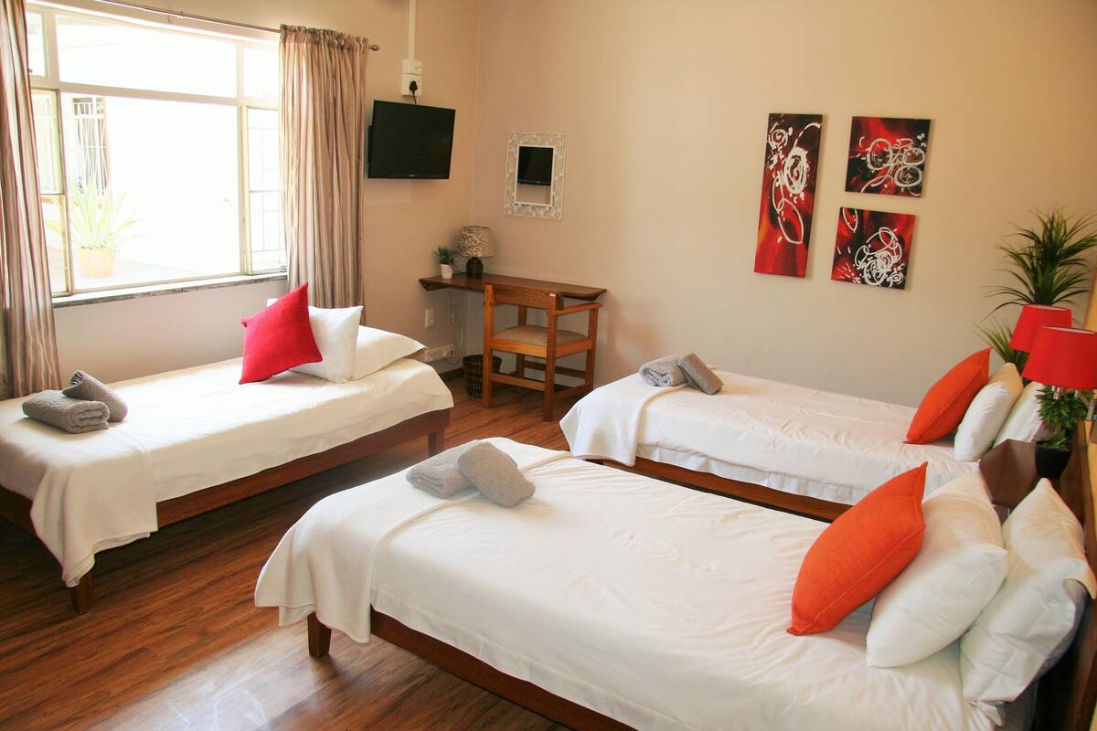 A hotel room with two single beds, a desk, a chair, and a TV on the wall.