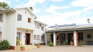 A two-story building with a covered patio area, potted plants, and solar panels on the roof. - Omaruru Guesthouse (Omaruru)