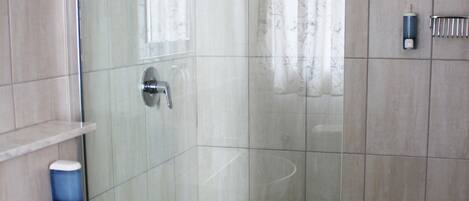 A bathroom with a glass-enclosed shower, a sink, and a tiled floor.
