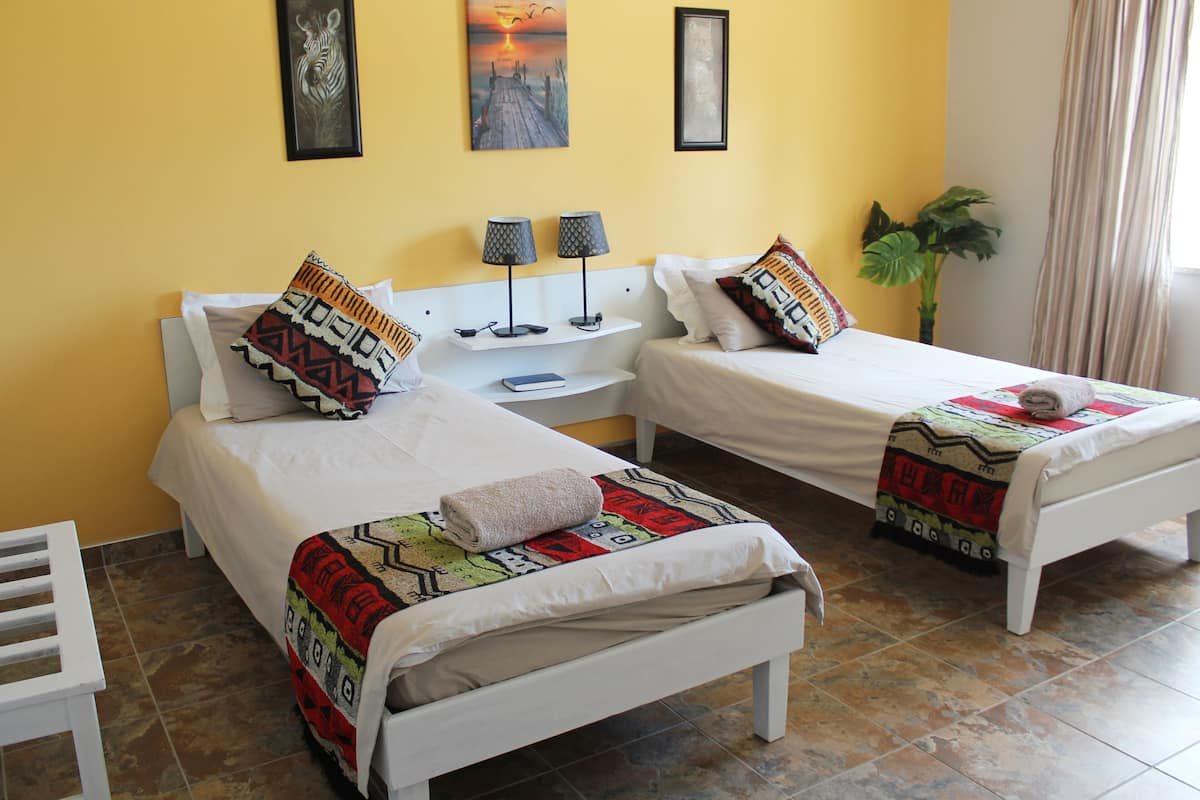A hotel room with two beds, a nightstand, a chair, and a potted plant.