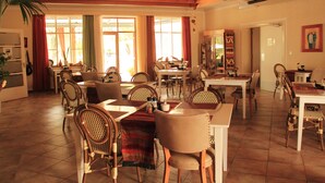 A spacious dining area with multiple tables and chairs, large windows with curtains, and a wooden ceiling. - Omaruru Guesthouse (Omaruru)