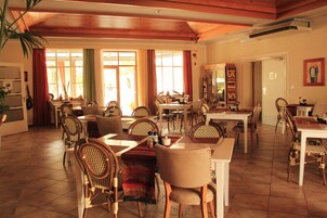 Un comedor amplio con varias mesas y sillas, ventanas grandes con cortinas y techo de madera.