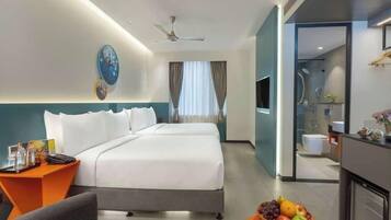 A hotel room with a bed, a desk, a chair, a TV, a shower area, and a fruit bowl.