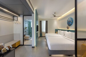 A hotel room with a bed, bedside tables, a TV, and a bathroom visible through an open door.