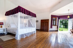 A bedroom with a four-poster bed, wooden flooring, and a view of a garden through an open door. - Scottish Planter Glendevon Bungalow (Walapane)