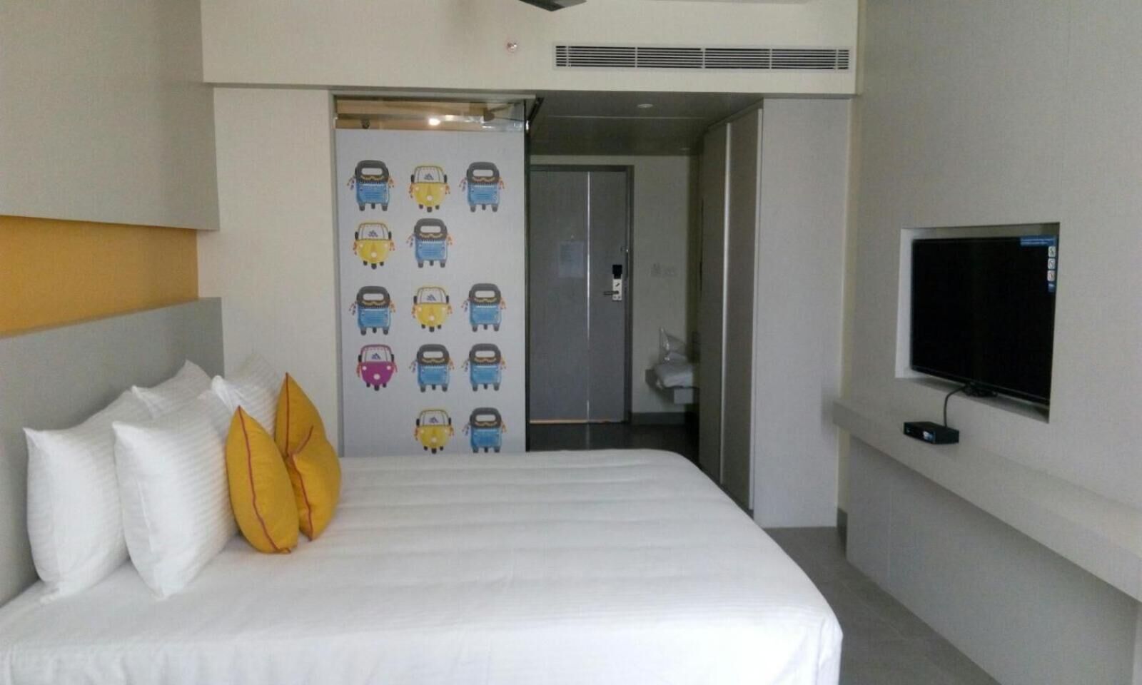 A hotel room with a bed, pillows, a TV, and a wall with a door.