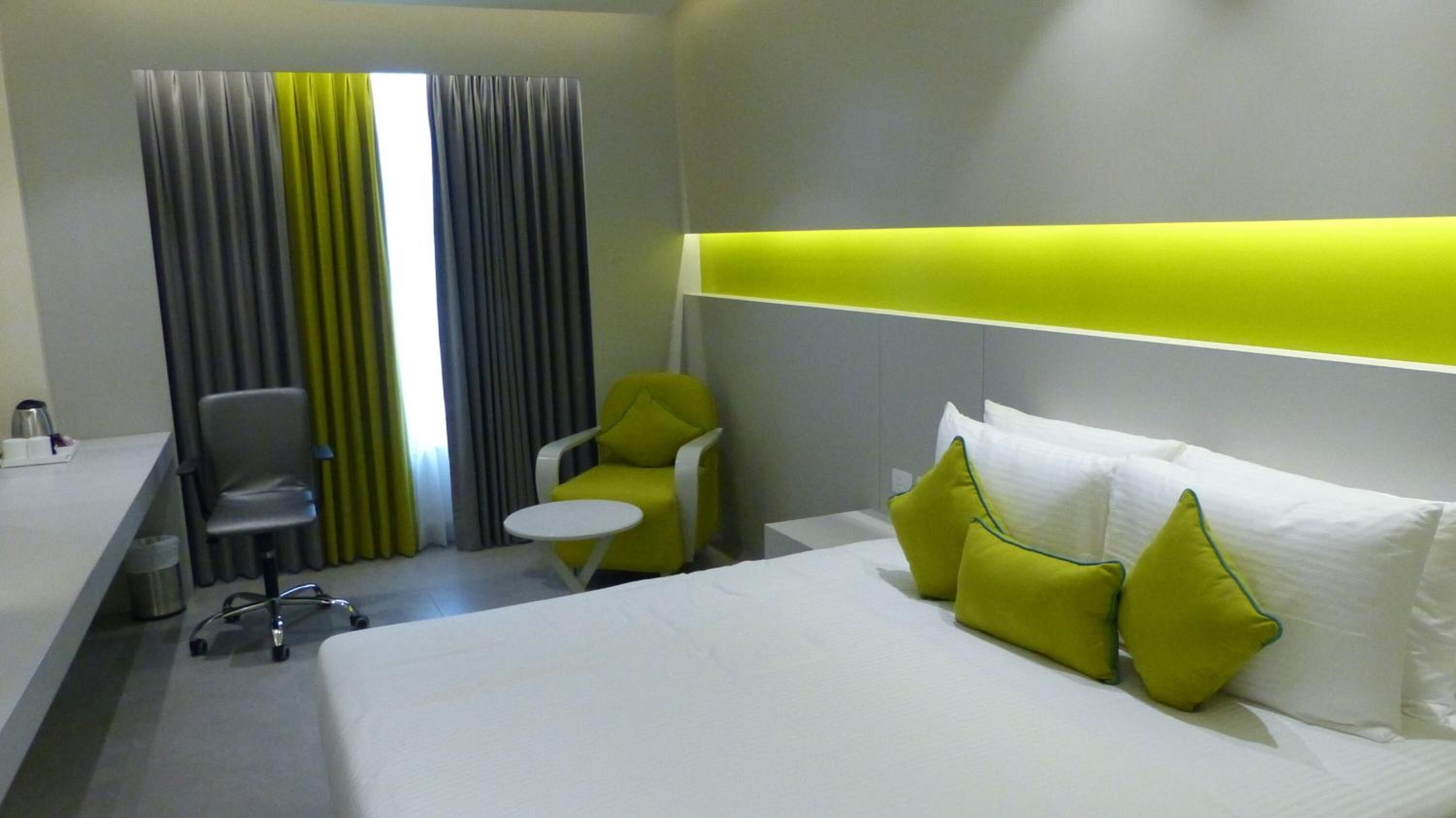 Een hotelkamer met een bed, twee stoelen, een klein tafeltje en een gordijn.