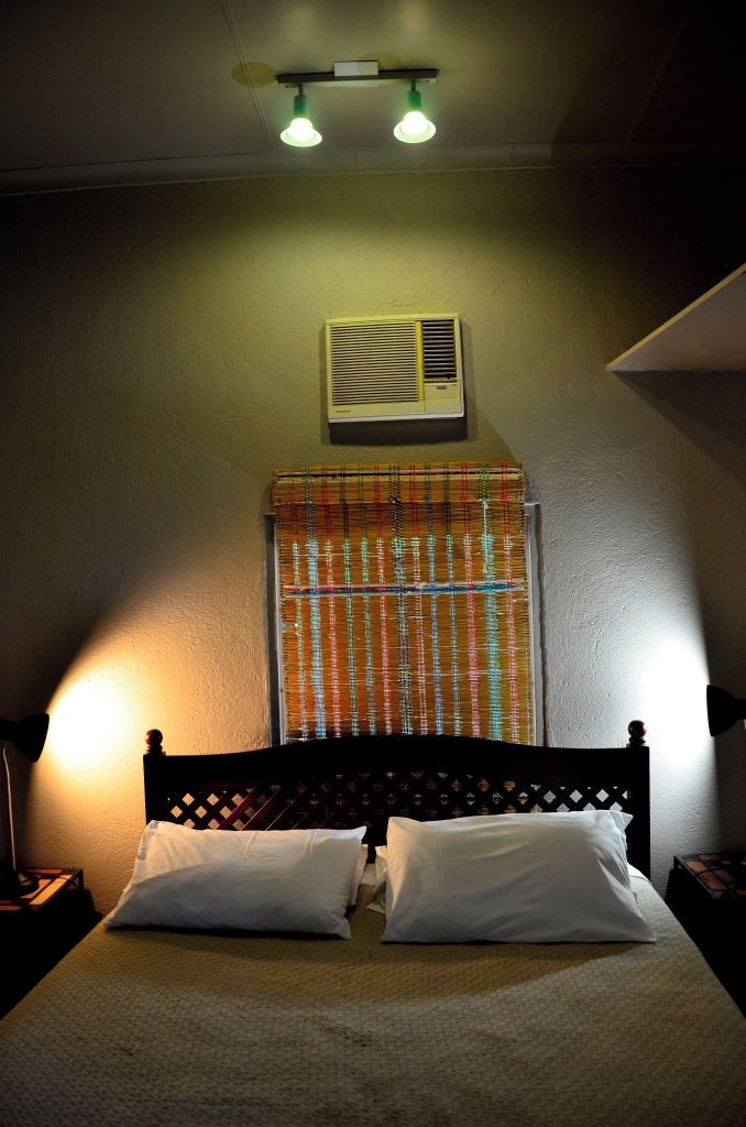 Un lit avec une tête de lit, une fenêtre avec un rideau à motifs et un climatiseur fixé au mur.