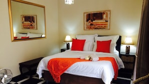 A hotel room with a checkered floor, a bed with white and red bedding, two bedside lamps, a mirror, and artwork on the walls. - Helderberg Guesthouse (Cape Town)