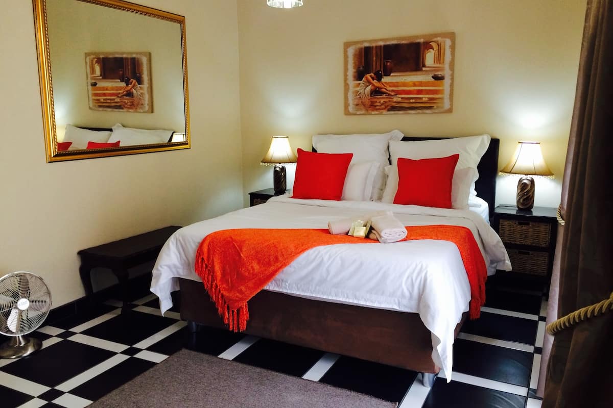 Une chambre d’hôtel avec un sol à carreaux, un lit avec une literie blanche et rouge, deux lampes de chevet, un miroir et des œuvres d’art accrochées aux murs.