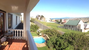 A balcony with a view of a swimming pool, a street, and distant mountains. - Helderberg Guesthouse (Cape Town)