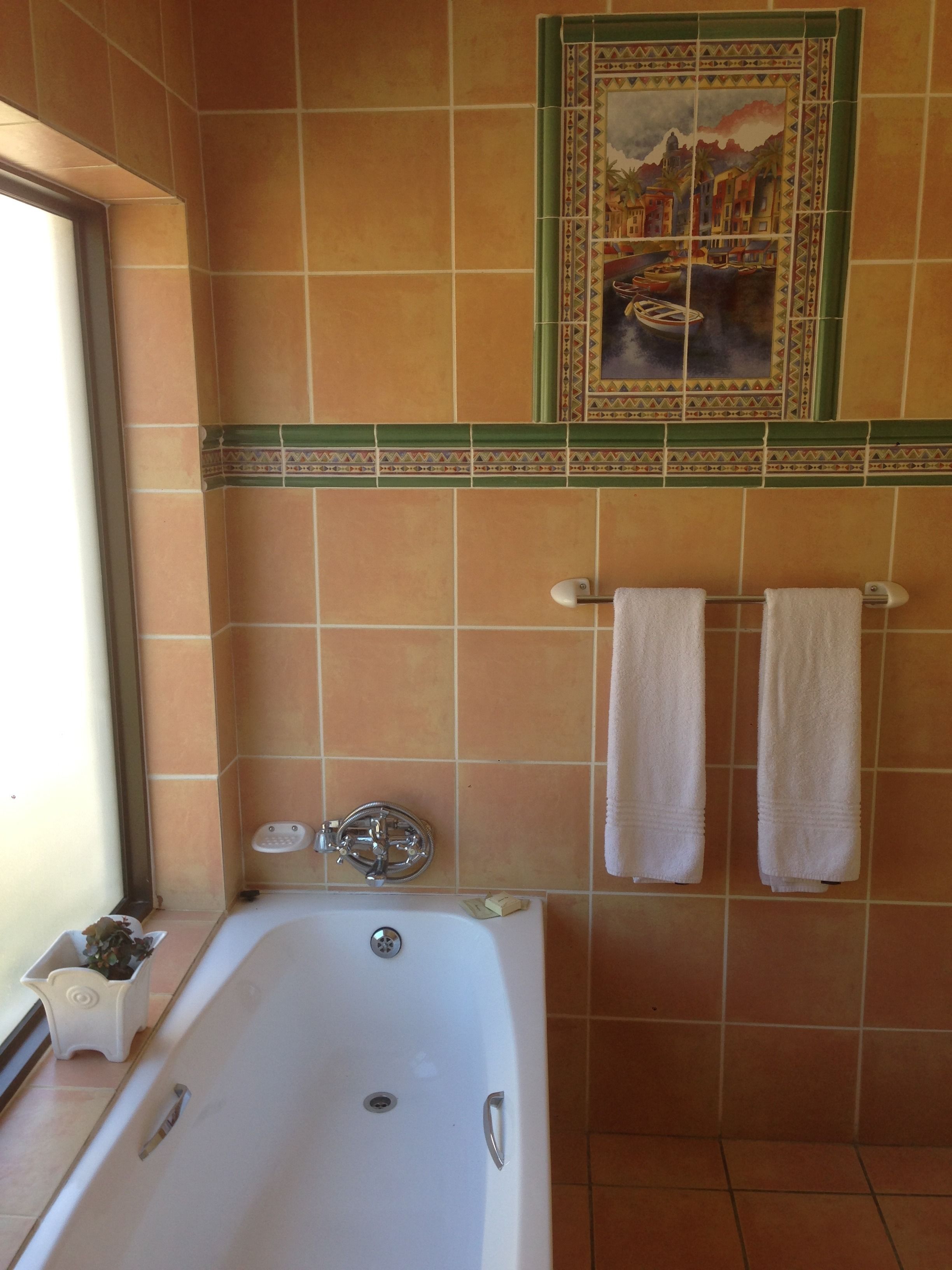 Un baño con bañera, dos toallas colgadas en un perchero y un mural decorativo de azulejos sobre la bañera.