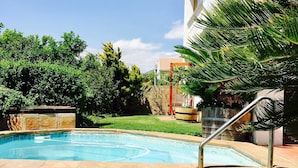 A swimming pool with a stone deck, surrounded by grass and trees. - Helderberg Guesthouse (Cape Town)