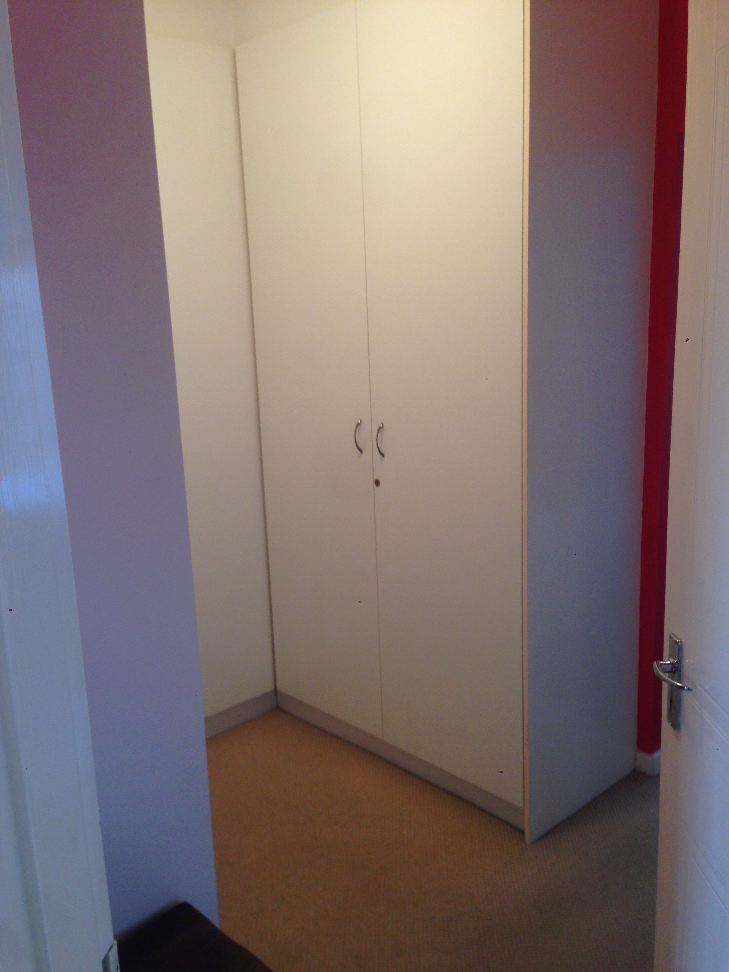 A room with a white wardrobe, a red door, and a beige carpet.