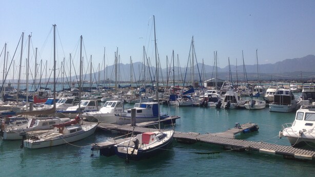 A marina with numerous boats docked at wooden piers, surrounded by calm water and distant mountains. - Helderberg Guesthouse (Cape Town)