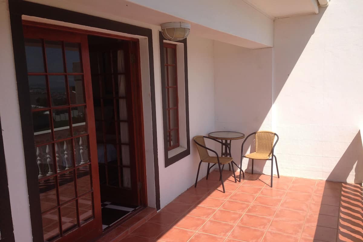 Une petite terrasse avec une table et des chaises, une porte avec des panneaux de verre et un luminaire fixé au mur.
