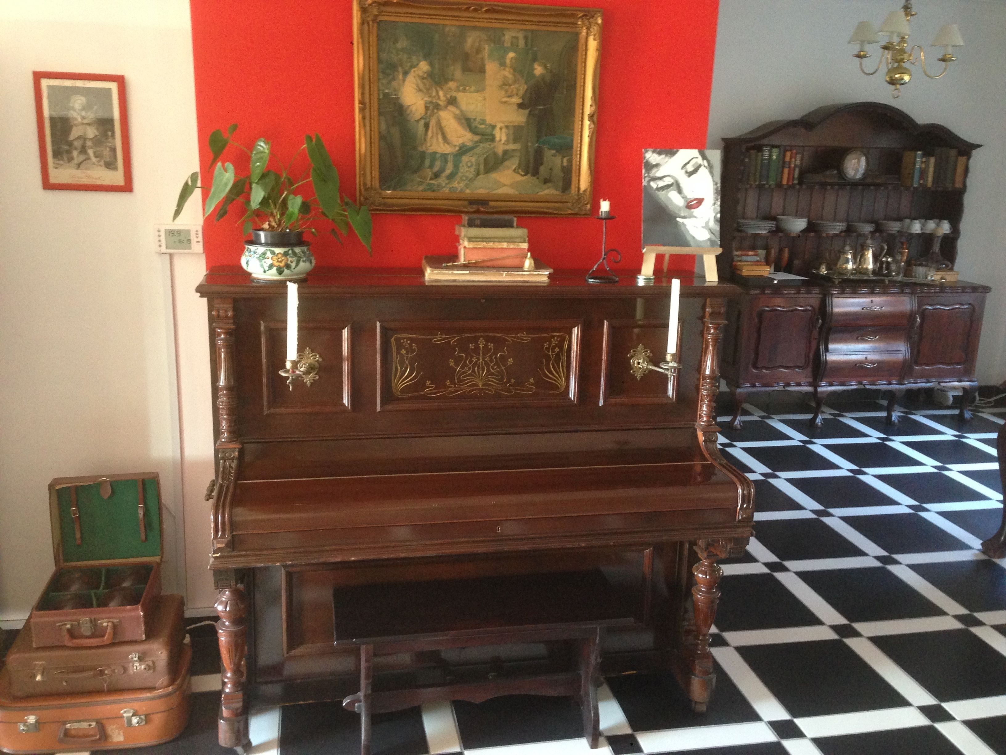 Una habitación con un piano de madera, una maleta verde y una estantería antigua.